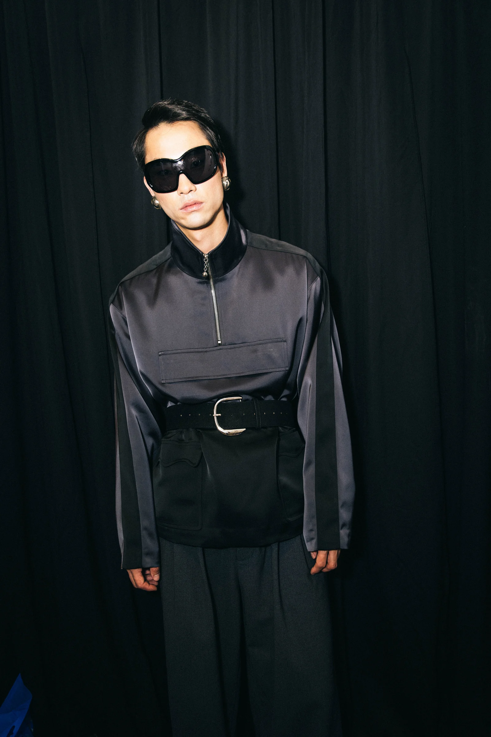 Private Policy — A model wearing sunglasses and a black belted outfit